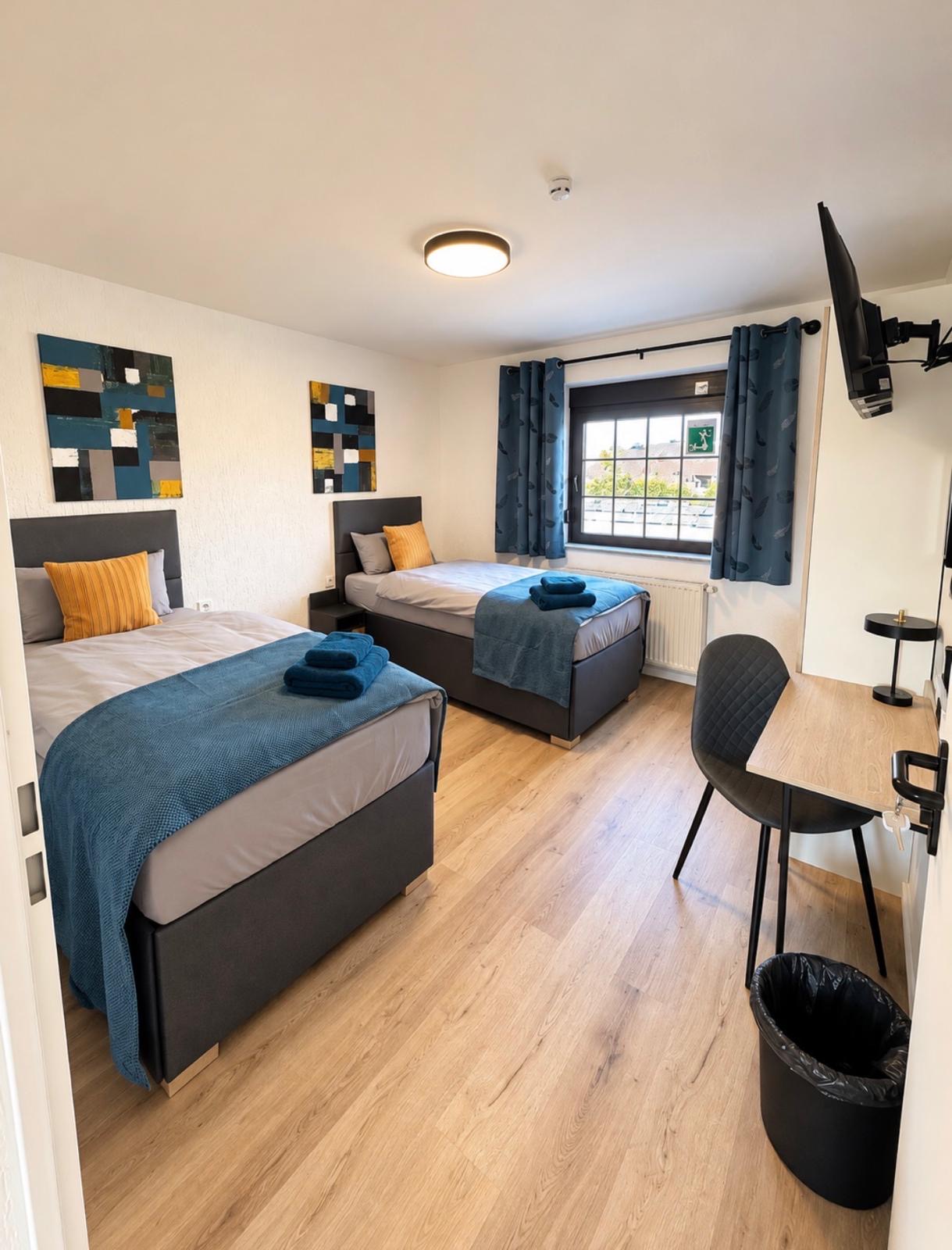 Modernes Zweibettzimmer mit Schreibtisch und Smart-TV